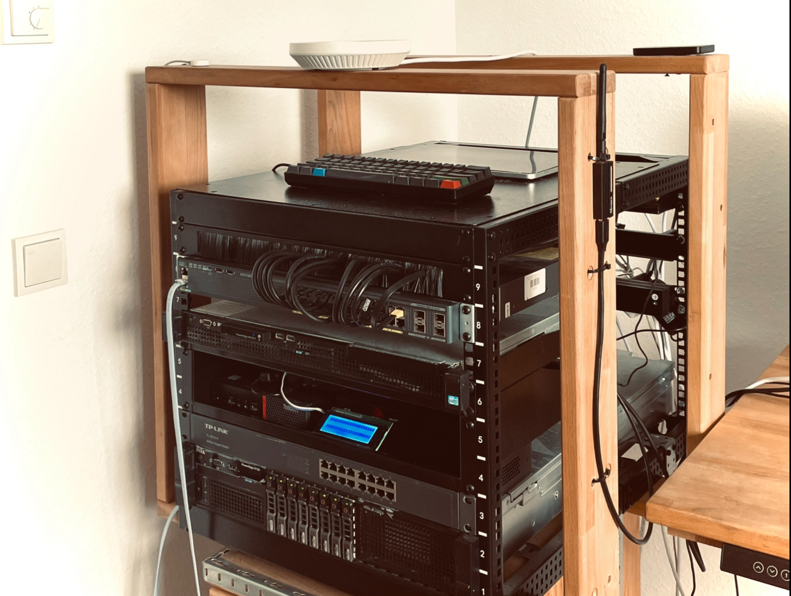 Home lab server setup with wooden rack holding Dell PowerEdge servers, Cisco switch, TP-Link AccessPoint with network cables, and a laptop